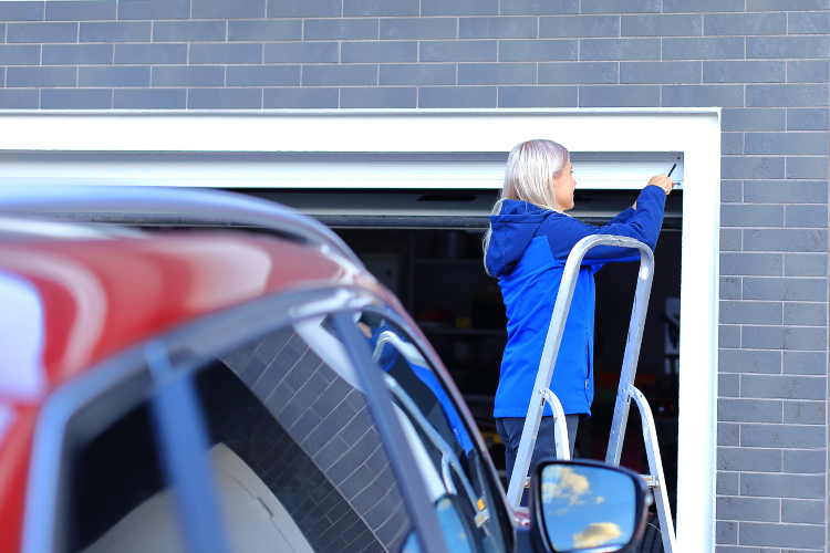 Žena popravlja pokvarena vrata na svojoj garaži